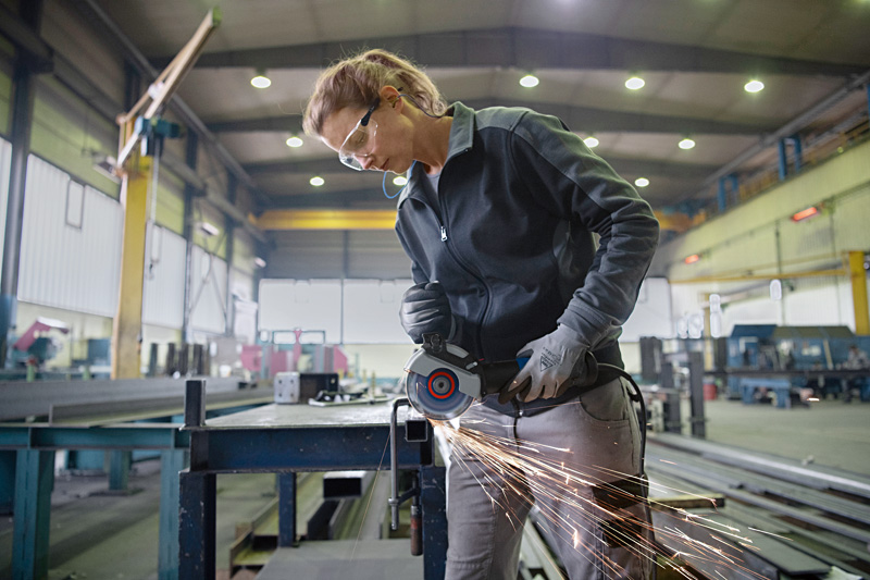 Eine Person mit Schutzausrüstung schleift Metall auf einer Werkbank und erzeugt dabei Funken. Anwendungsbild